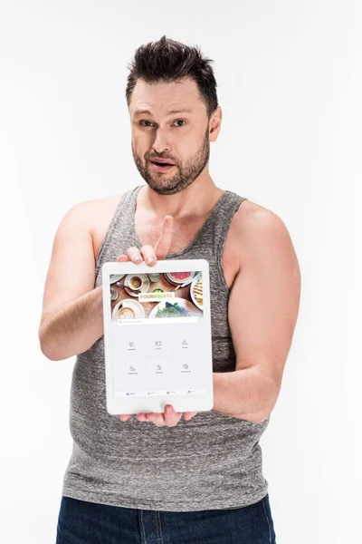 Hombre con sobrepeso mirando a la cámara y mostrando tableta digital con aplicación cuadrada en la pantalla aislada en blanco - foto de stock