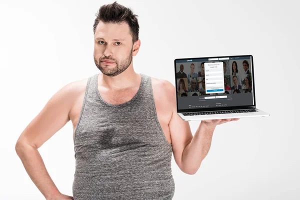 Hombre con sobrepeso mirando a la cámara y la celebración de la computadora portátil con linkedin sitio web en la pantalla aislada en blanco - foto de stock