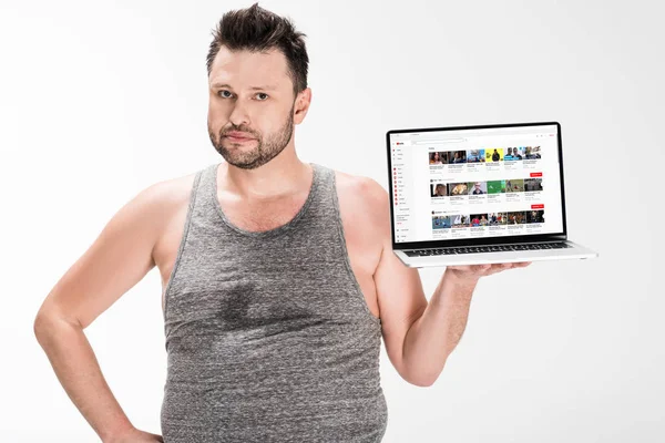 Übergewichtiger Mann schaut in Kamera und hält Laptop mit Youtube-Website auf Bildschirm isoliert auf weiß — Stockfoto