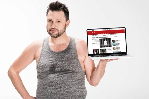 Overweight man looking at camera and holding laptop with bbc news website on screen isolated on white — Stock Photo