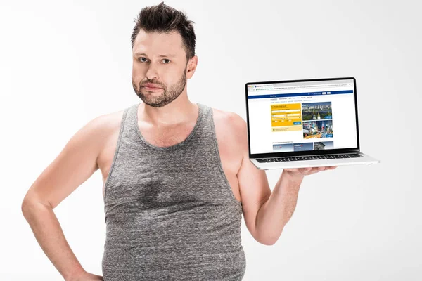 Übergewichtiger Mann blickt in Kamera und hält Laptop mit Buchungswebseite auf dem Bildschirm isoliert auf weiß — Stockfoto