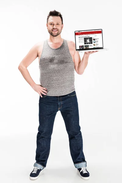Улыбающийся человек с избыточным весом, смотрящий в камеру и представляющий ноутбук с новостным сайтом bbC на экране, изолированным на белом — стоковое фото