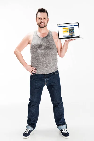 Souriant homme en surpoids regardant la caméra et présentant ordinateur portable avec site de réservation à l'écran isolé sur blanc — Photo de stock