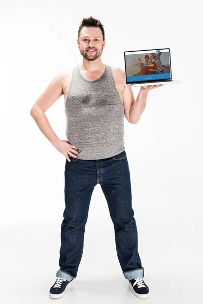 Sorrindo homem com excesso de peso olhando para a câmera e apresentando laptop com site couchsurfing na tela isolada no branco — Fotografia de Stock