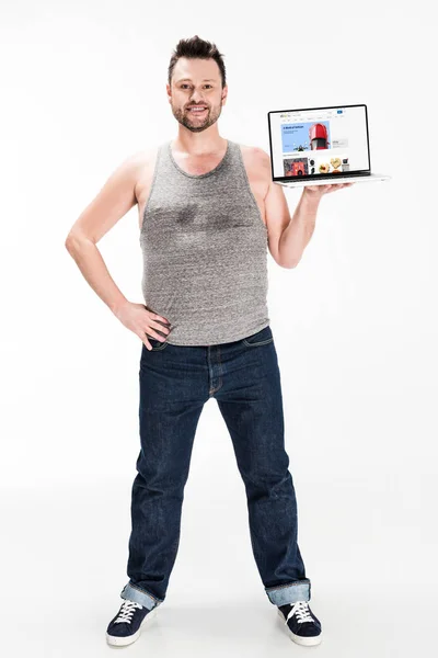 Souriant homme en surpoids regardant la caméra et présentant ordinateur portable avec site Web ebay à l'écran isolé sur blanc — Photo de stock