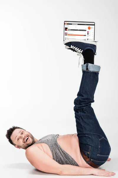 Excited overweight man looking at camera and holding with legs laptop with soundcloud website on screen — Stock Photo