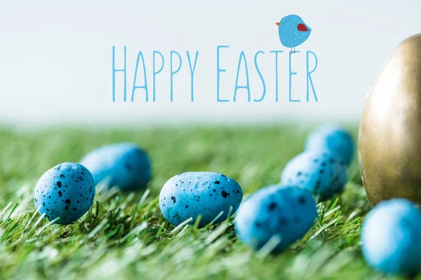 Blue painted quail eggs on green grass near golden chicken egg and happy Easter lettering — Stock Photo