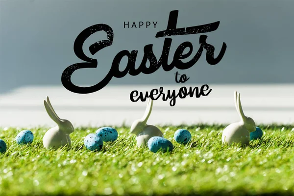 Conigli decorativi su erba verde vicino alle uova di quaglia blu con felice Pasqua a tutti illustrazione — Foto stock