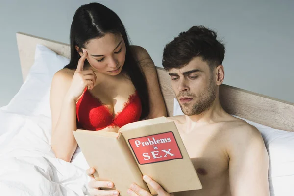 Concentrado multicultural casal leitura problemas no livro de sexo enquanto deitado na cama sob a luz do sol — Fotografia de Stock