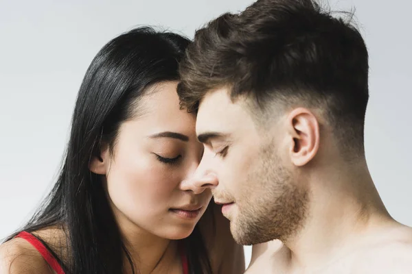 Beautiful asian woman with handsome pensive boyfriend standing face to face with closed eyes on grey — Stock Photo