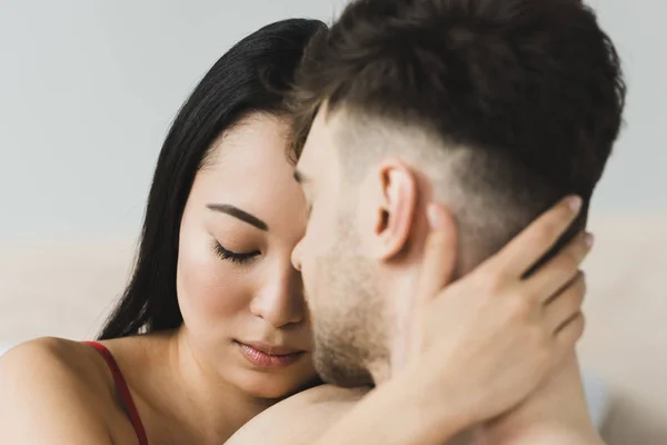 Selektiver Fokus der schönen, nachdenklichen asiatischen Frau, die ihren Freund mit geschlossenen Augen umarmt — Stockfoto