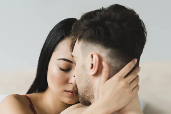 Hermosa, mujer asiática pensativa con los ojos cerrados abrazando novio - foto de stock