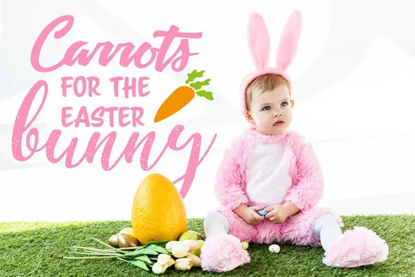 Cute baby in bunny costume sitting near colorful chicken eggs, tulips and yellow ostrich egg with carrots for the Easter bunny illustration — Stock Photo