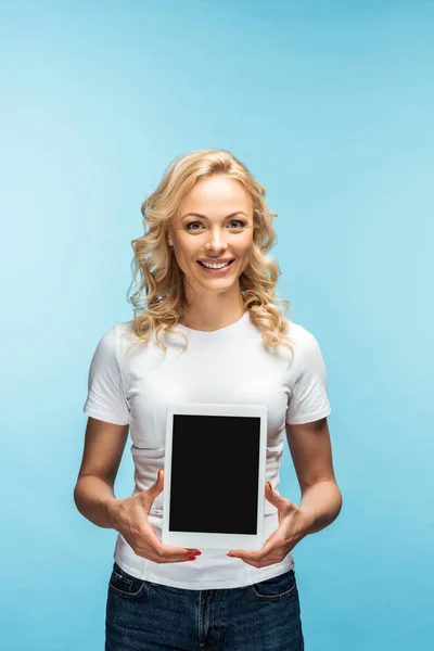 Happy blonde woman looking at camera while holding digital tablet with blank screen on blue — Stock Photo