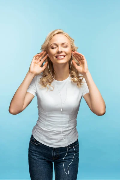 Весела жінка з закритими очима слухає музику в навушниках на синьому — стокове фото
