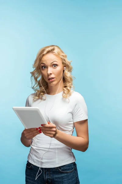 Mujer sorprendida sosteniendo la tableta digital mientras escucha música en azul - foto de stock