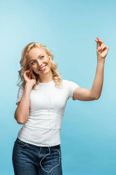 Mulher feliz ouvindo música em fones de ouvido enquanto gesticulando em azul — Fotografia de Stock