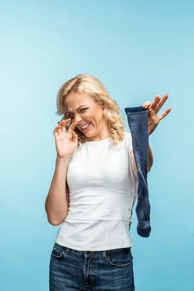 Attractive curly blonde woman looking at smelly dirty sock on blue — Stock Photo