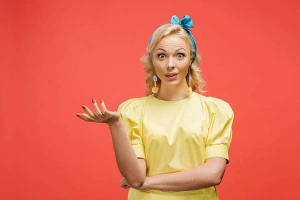 Femme blonde surprise en bandeau bleu regardant la caméra et gesticulant sur rouge — Photo de stock