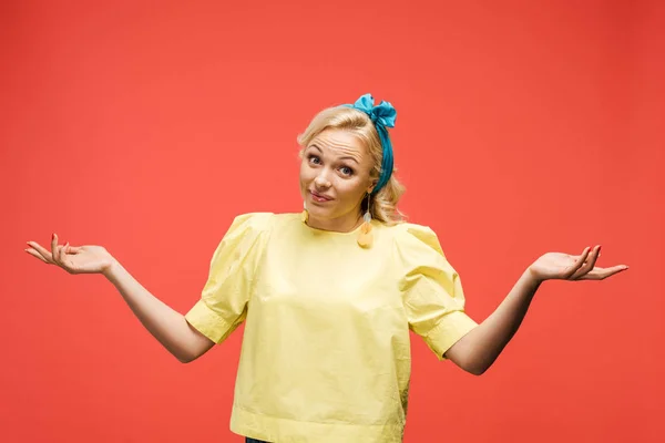 Смущенная блондинка в синем повязке стоящая и жестикулирующая на красном — стоковое фото