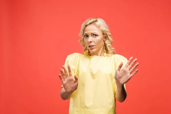 Scared curly blonde woman looking at camera and gesturing on red — Stock Photo