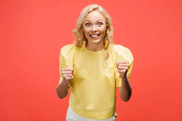 Happy blonde woman looking at camera and celebrating success on red — Stock Photo