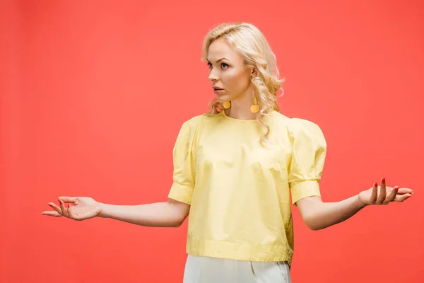 Спантеличена блондинка стоїть з простягнутими руками на червоному — стокове фото