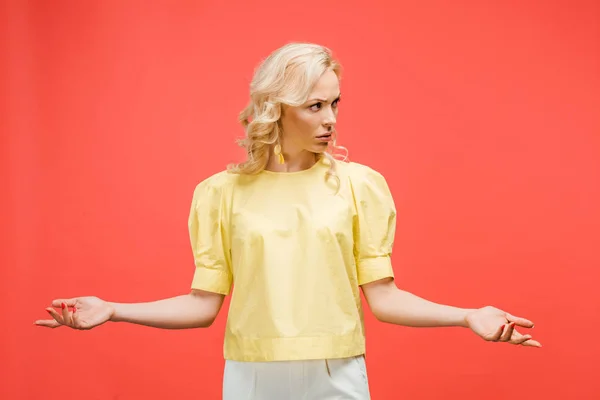 Confused curly blonde woman standing with outstretched hands on red — Stock Photo