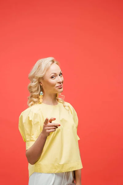 Heureuse femme blonde regardant caméra et pointant du doigt sur rouge — Photo de stock