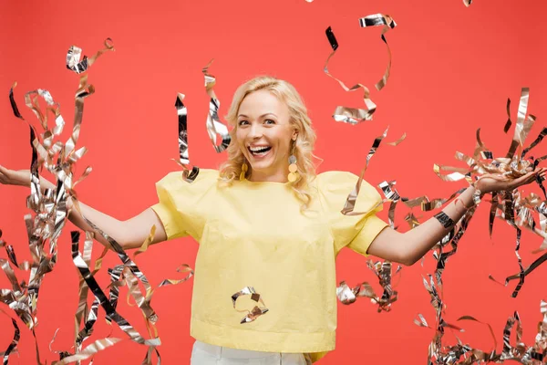 Glückliche blonde Frau lächelt neben silbrig funkelndem Konfetti auf Rot — Stockfoto