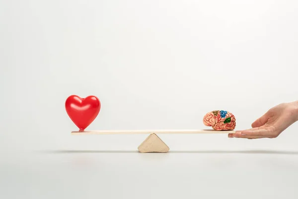 Cropped view of woman holding seesaw with human brain and red heart on white — Stock Photo