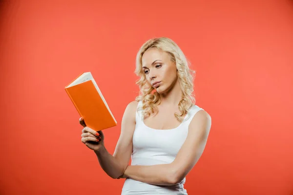 Attractive curly blonde woman reading book while standing on red — Stock Photo