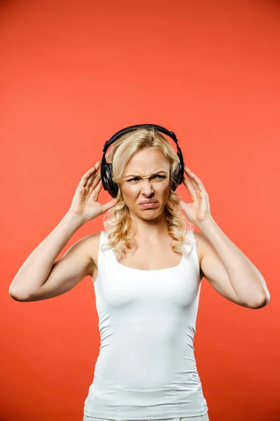 Displeased blonde woman listening music in headphones on red — Stock Photo