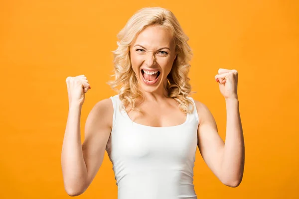 Mujer rubia emocionada mirando a la cámara y celebrando triunfo aislado en naranja - foto de stock