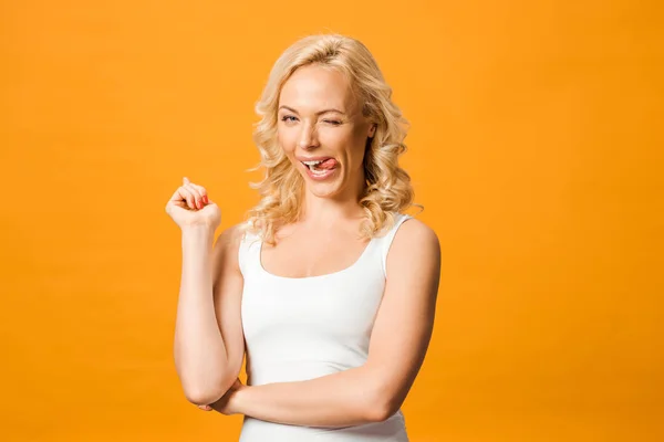 Счастливая блондинка, демонстрирующая язык, глядя в камеру, изолированную от апельсина — стоковое фото