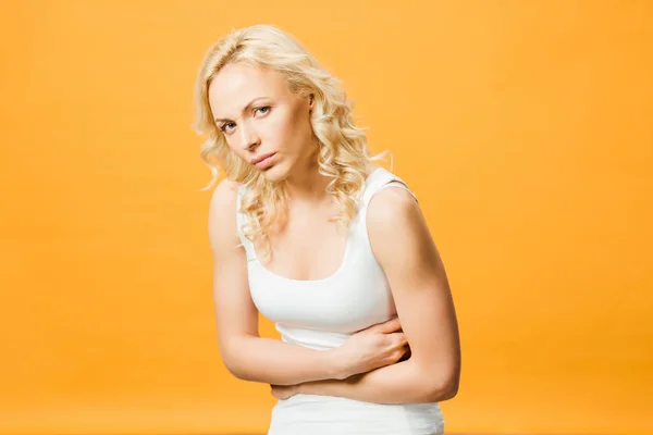 Mujer molesta mirando a la cámara mientras tiene dolor de estómago aislado en naranja - foto de stock