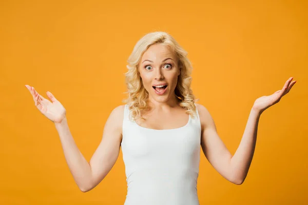 Mujer rubia sorprendida haciendo gestos y mirando a la cámara aislada en naranja - foto de stock