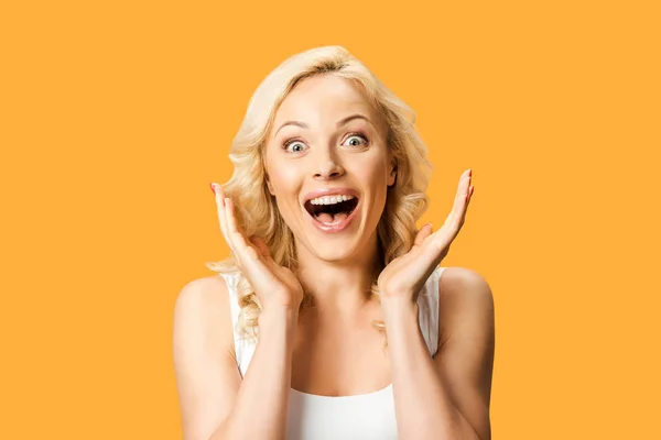 Surprised curly woman gesturing and looking at camera isolated on orange — Stock Photo