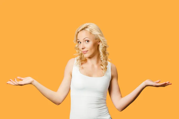 Jolie femme blonde bouclée montrant geste haussant les épaules isolé sur orange — Photo de stock