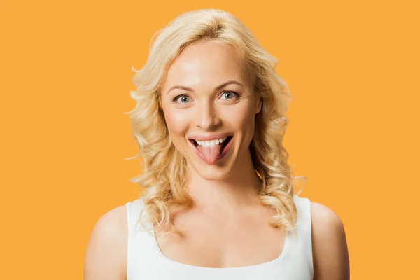 Smiling blonde woman showing tongue and looking at camera isolated on orange — Stock Photo