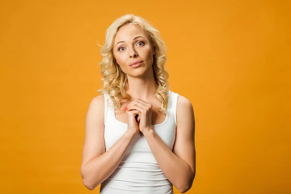 Pretty curly woman looking at camera and standing with clenched hands isolated on orange — Stock Photo