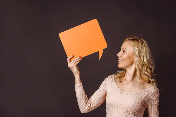 Attraktive blonde Frau hält orangefarbene Sprechblase isoliert auf schwarz — Stockfoto