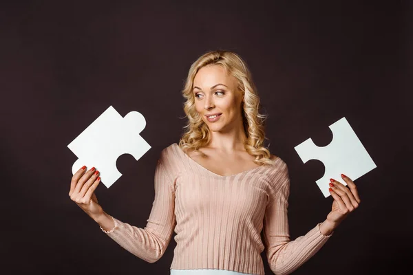 Happy blonde woman holding jigsaw pieces isolated on black — Stock Photo