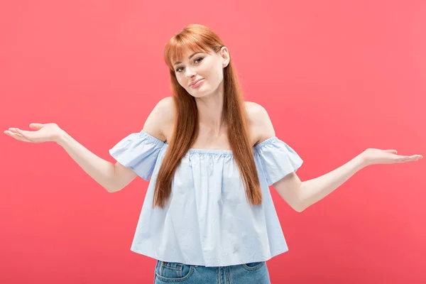 Surprised redhead girl showing shrug gesture and looking at camera isolated on pink — Stock Photo