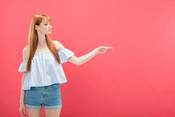 Redhead woman in denim shorts pointing with finger isolated on pink — Stock Photo