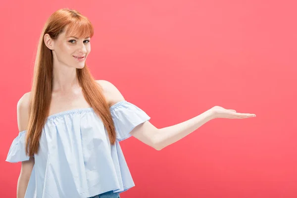 Sourire rousse femme pointant avec la main et regardant la caméra isolée sur rose — Photo de stock