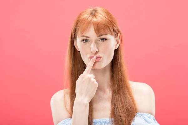 Front view of curious redhead girl looking at camera and touching lips with finger isolated on pink — Stock Photo