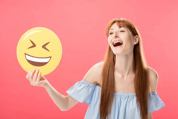 KYIV, UKRAINE - MAY 23, 2019: excited redhead girl holding laughing smiley isolated on pink — Stock Photo