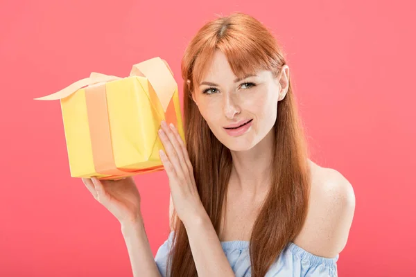 Curiosa ragazza rossa compleanno in possesso di scatola regalo gialla con nastro isolato su rosa — Foto stock