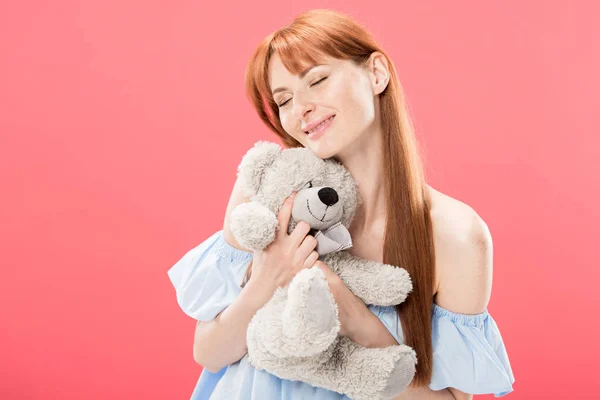 Rousse souriante jeune femme tenant ours en peluche isolé sur rose — Photo de stock